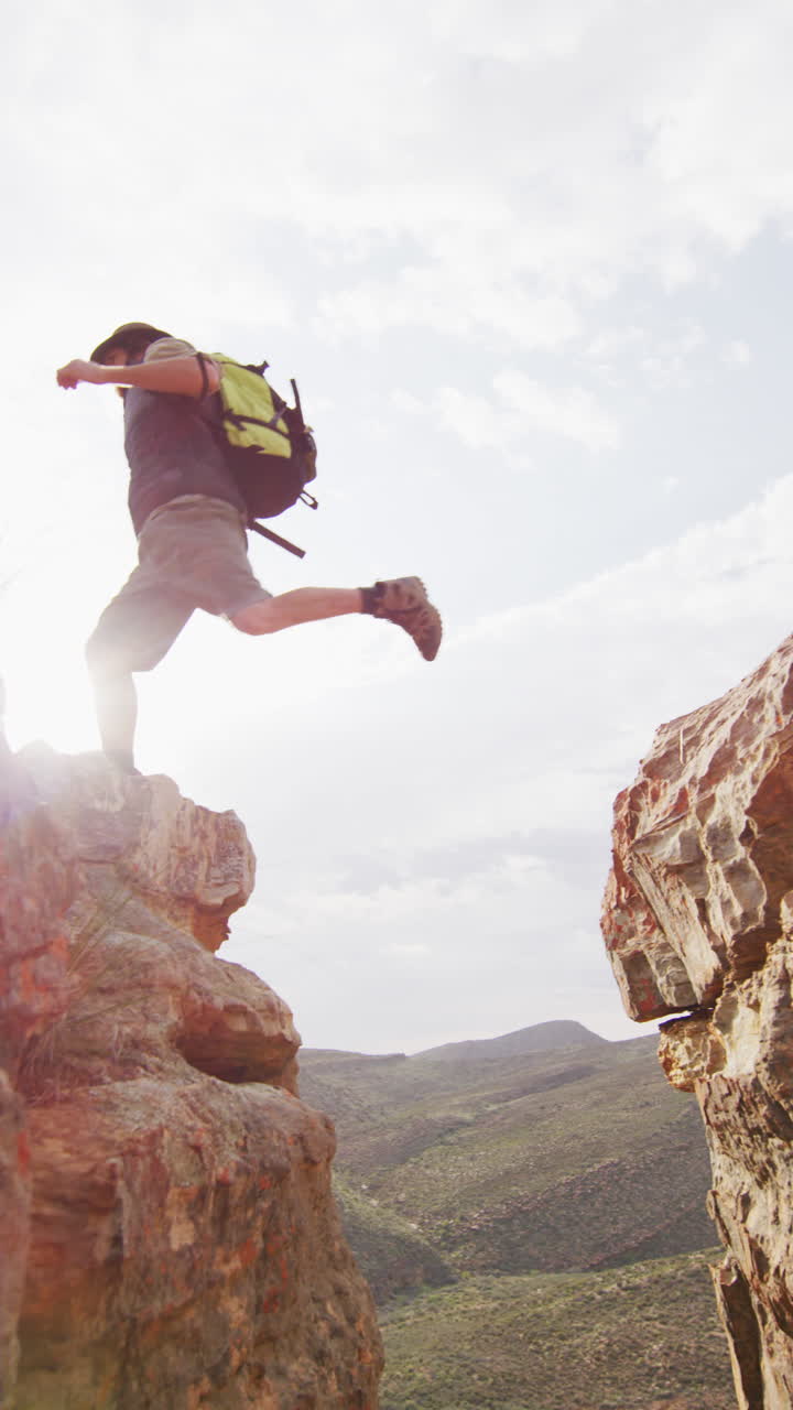 video vertical de un sobreviviente caucásico barbudo explorando el desierto saltando a través de un barranco