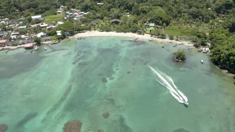 aerial tilts down to a boat driving along the beach coast