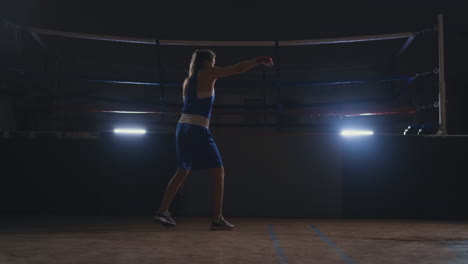 A-beautiful-woman-conducts-a-shadow-fight-while-practicing-hard-for-future-victories.-Dark-gym-background.-steadicam-shot