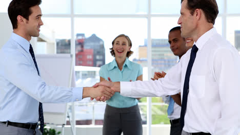 los hombres de negocios se dan la mano mientras otros hombres de negocios aplauden