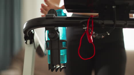 running woman takes water bottle on treadmill at home closeup. thirsty lady drinks to refresh on hard cardio workout with machine in house. sports routine