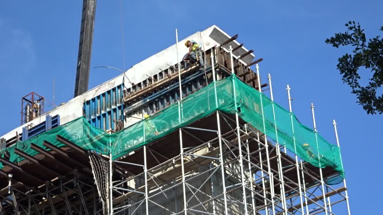 Construction workers working at height installing reinforcement bar and form work at the construction site. They are requested to wear appropriate safety gear to prevent bad happen to them.