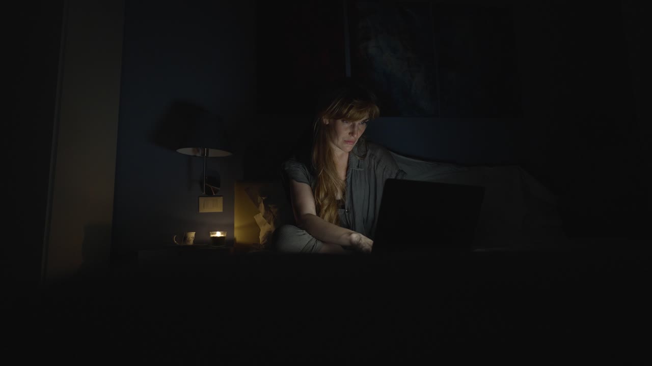 Student studying late at night in her bed at home, the woman is tired from a long day of work