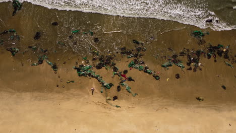 Vietnam-tropical-beach-filled-with-plastic-fishing-net-washed-out-after-typhoon-during-monsoon-season,-consequence-of-climate-change-disasters-and-displacement,-aerial-ocean-view