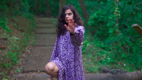 Young-Woman-in-Purple-Dress-and-Painted-Lips-Posing-Showing-Palm-of-the-Hand,-Path-in-Background