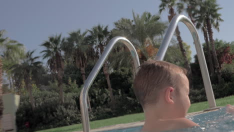 niño alegre salpicando agua en la piscina al aire libre