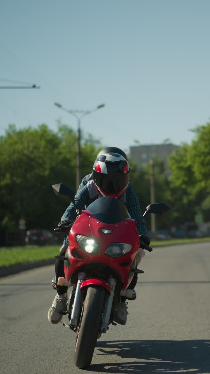 dos amigos montan una bicicleta eléctrica roja, ambos con cascos, navegando por la carretera con coches estacionados a lo largo de la carretera, postes eléctricos y árboles exuberantes son visibles en el fondo