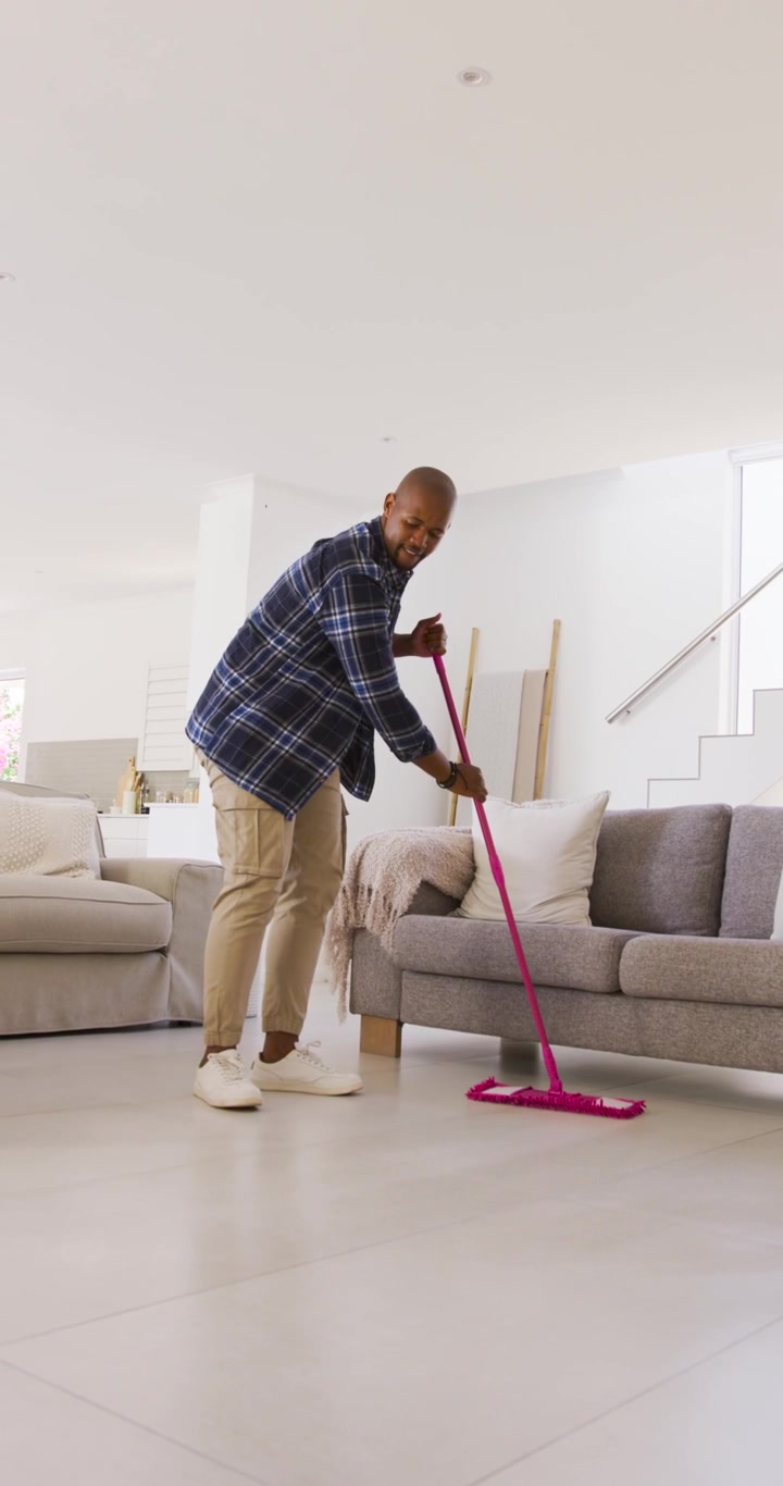 Mann plasserer rosa mopphode på fliser og mopper mot sofaer, med smale bevegelser for hjemmerengjøring