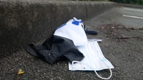 Dirty-discarded-used-corona-virus-masks-and-gloves-litter-on-road-blowing-in-wind-with-copy-space-dolly-right