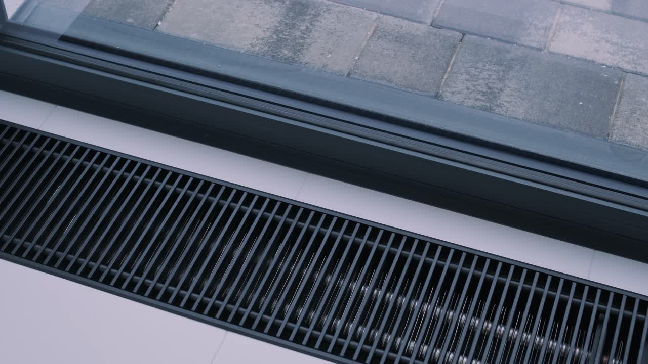 An up-close view of a modern, clean-lined HVAC floor register near a window, blending seamlessly with the sleek interior design