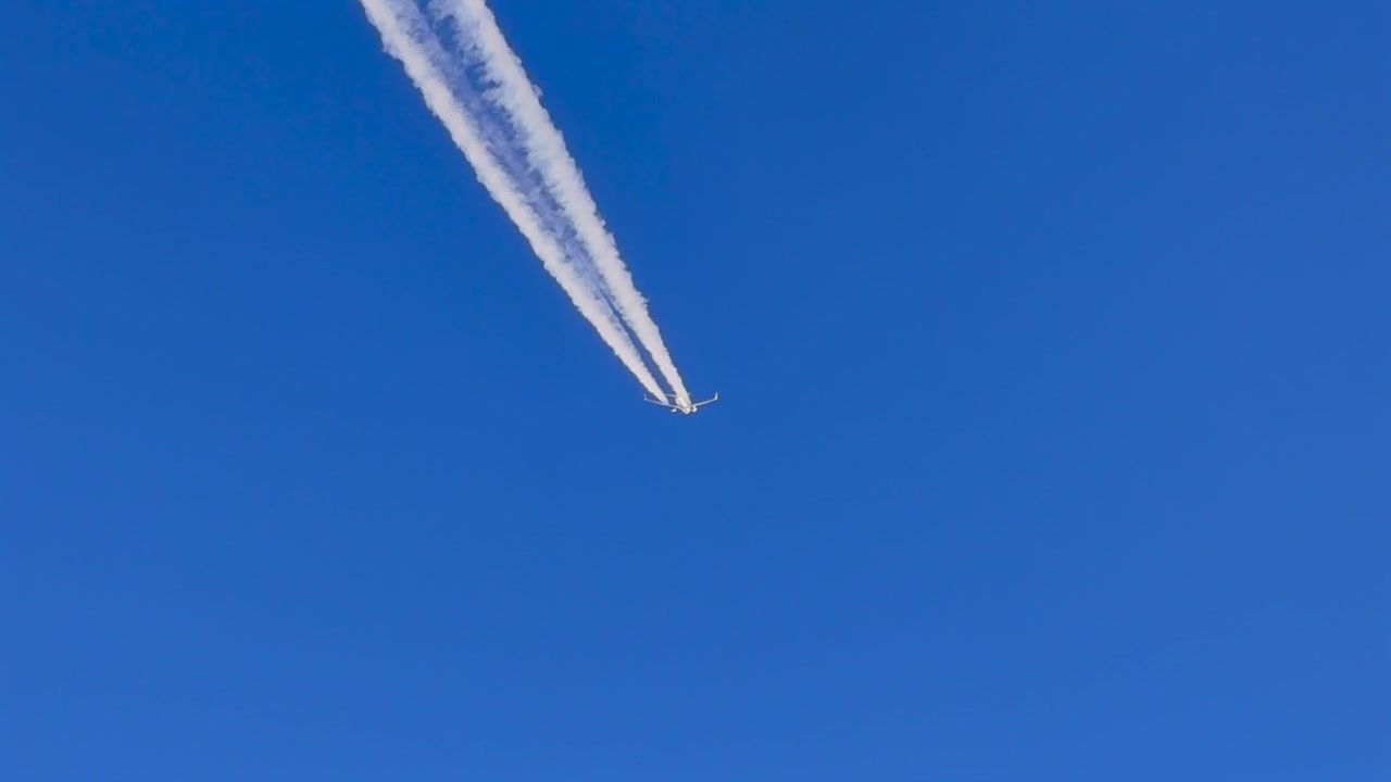 Vue du pilote d'un avion à réaction laissant une traînée de condensation s'estompant dans un ciel bleu intense, prise depuis un autre jet volant 600m plus bas