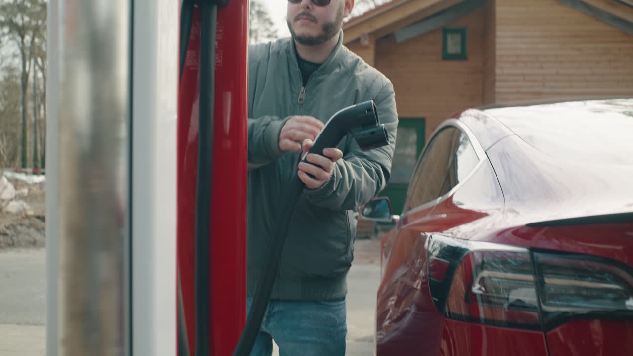 Man finishes charging the electric car, closes the charging door and puts away the charging cable