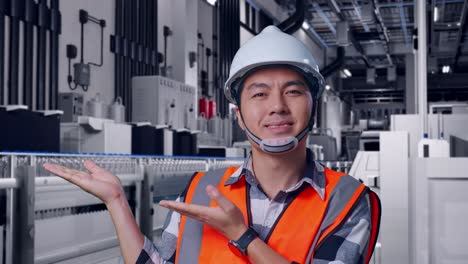 close up of asian male engineer with safety helmet smiling and pointing to side while standing with water production in bottling factory