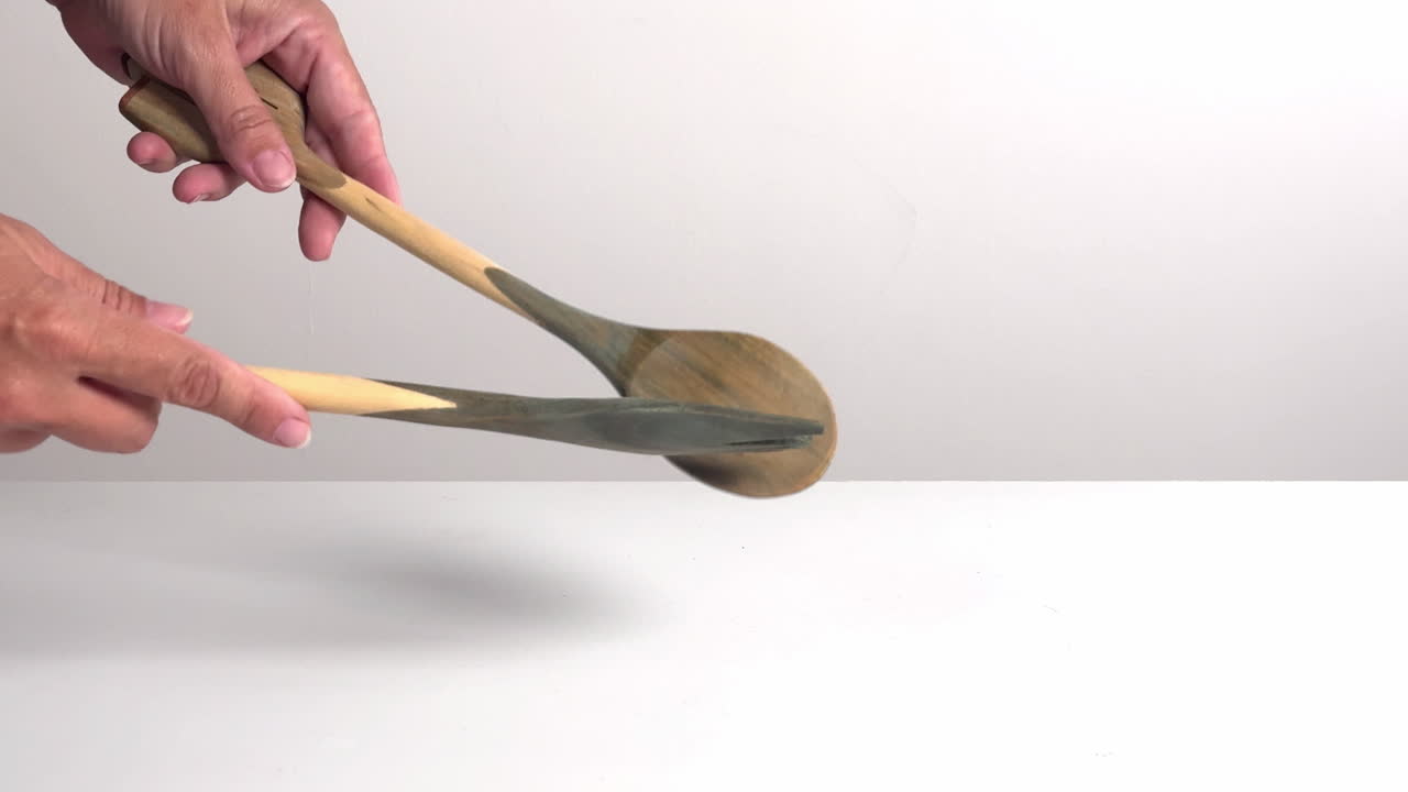 Hands Clacking Wooden Cooking Utensils Against a White Background