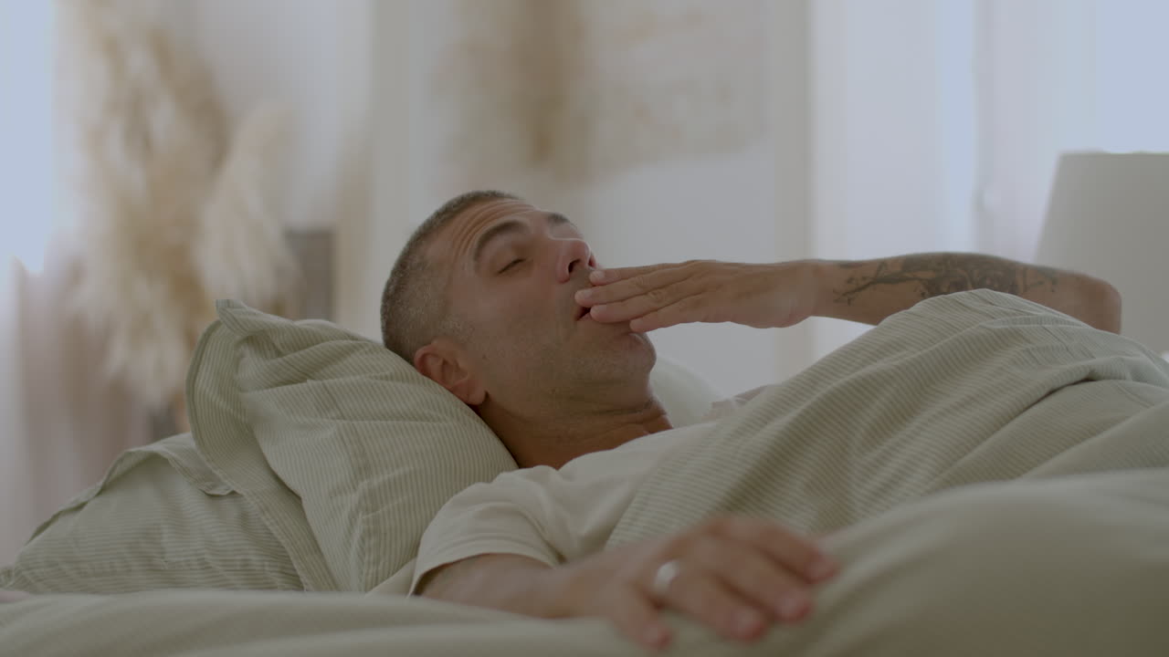 Uomo sereno sdraiato a letto, che si sveglia, si stiracchia e sbadiglia