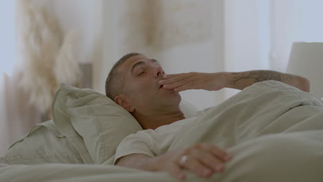 peaceful man lying in bed, waking up, stretching and yawning