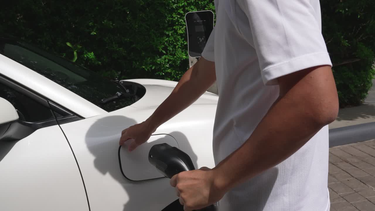 Ev şarj istasyonundan elektrikli aracına (EV) şarj kablosunu takan ilerici adam.