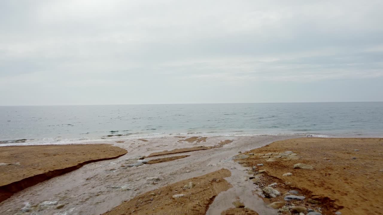 Footage along a river on a Jurassic Coast beach running through the sand leading out to the channel off the south coast of England, Dorset. Captured on a cloudy day.