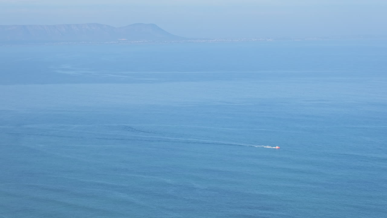 A small boat traverses a vast blue ocean with distant mountains