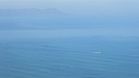 a small boat traverses a vast blue ocean with distant mountains