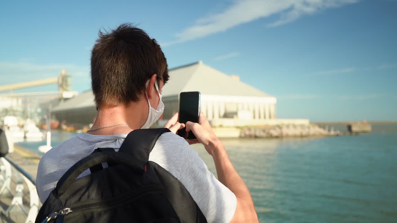 vista trasera de un hombre tomando fotos del mar azul en puerto ingeniero blanco, buenos aires, argentina