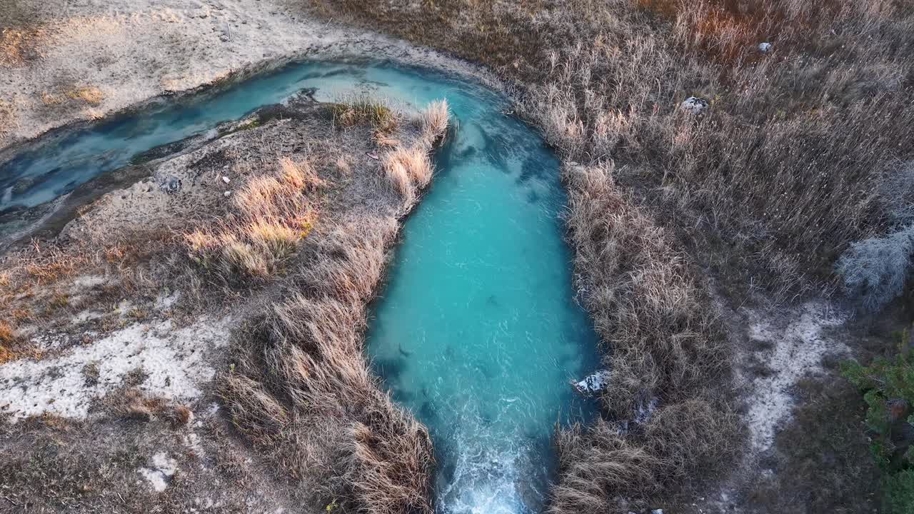 Aerial view of vibrant blue stream cutting through rugged dried vegetation in Michigan wilderness