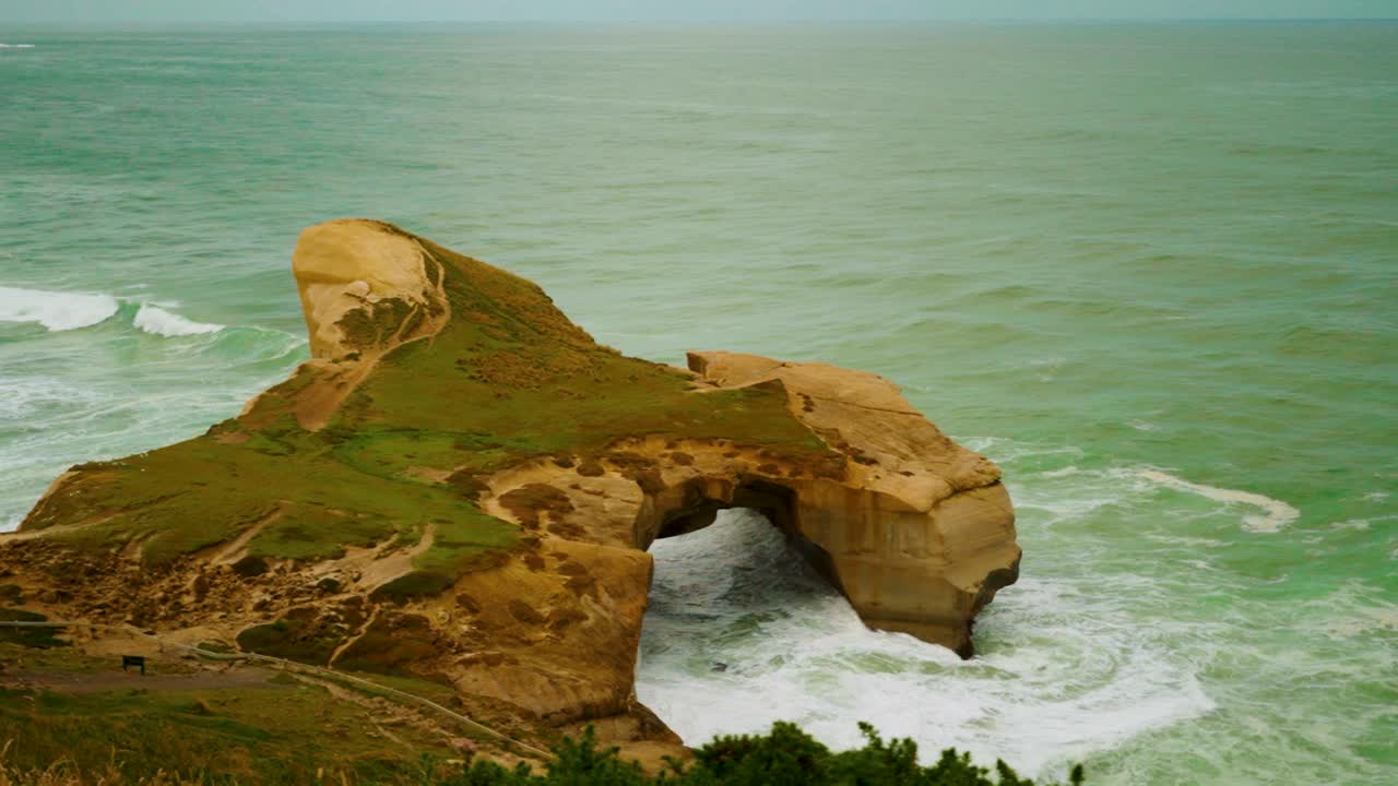 Walking handheld shot of a sea arch rock formation along the coast in New Zealand