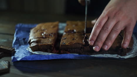 Man-slicing-cake-on-wooden-table.-Prepared-chocolate-cake-pieces-on-kitchen