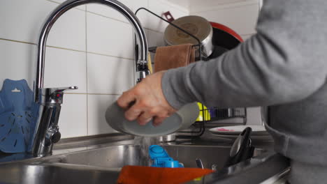 hombre irreconocible lavando platos en la cocina