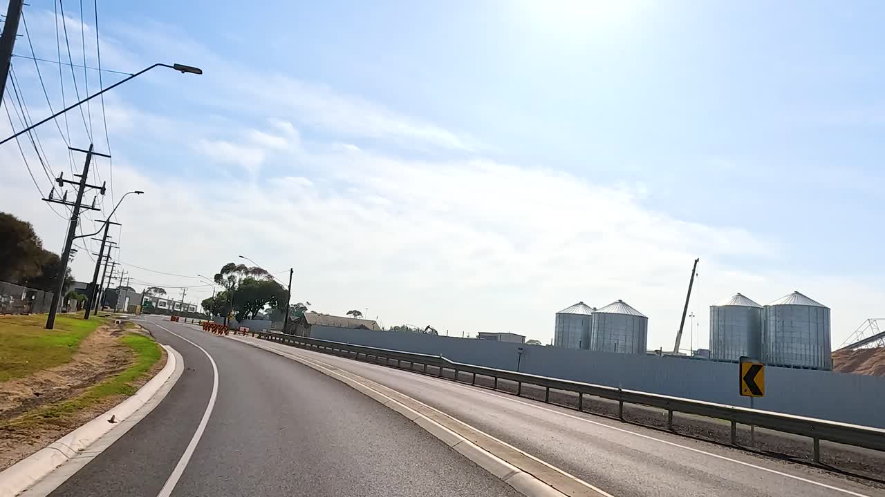 A smooth drive along a sunlit road in Geelong, showcasing industrial buildings and clear skies. The camera captures the serene environment