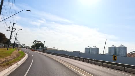 a smooth drive along a sunlit road in geelong, showcasing industrial buildings and clear skies. the camera captures the serene environment