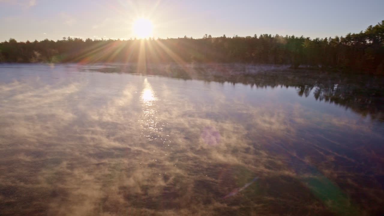 Cinematic aerial view of dawn mist hovering and rising over water