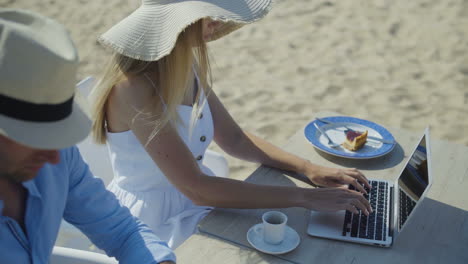 pareja joven usando computadoras portátiles en la playa