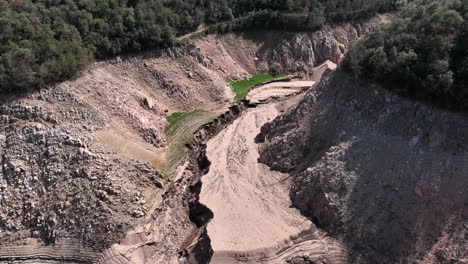 Aerial-view-descending-to-rocky-waterless-drought-gorge-of-Sau-reservoir,-Catalonia,-Spain