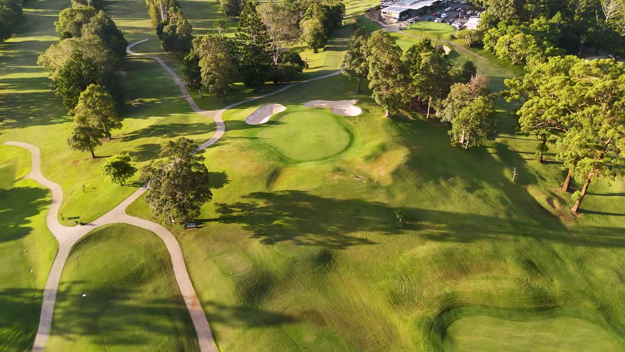 Drone footage captures a serene golf course landscape with vibrant greens and long shadows during sunset