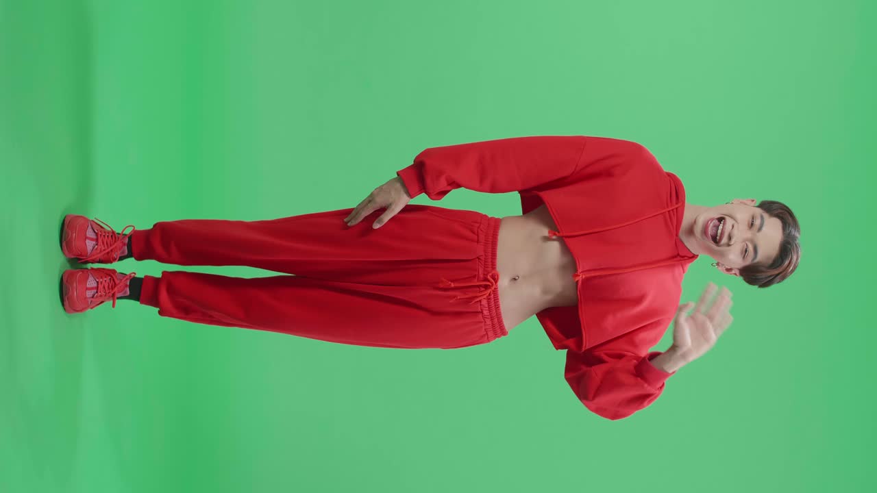Full Body Of Happy Asian Transgender Male Waving Hands And Looking At Camera In The Green Screen Studio