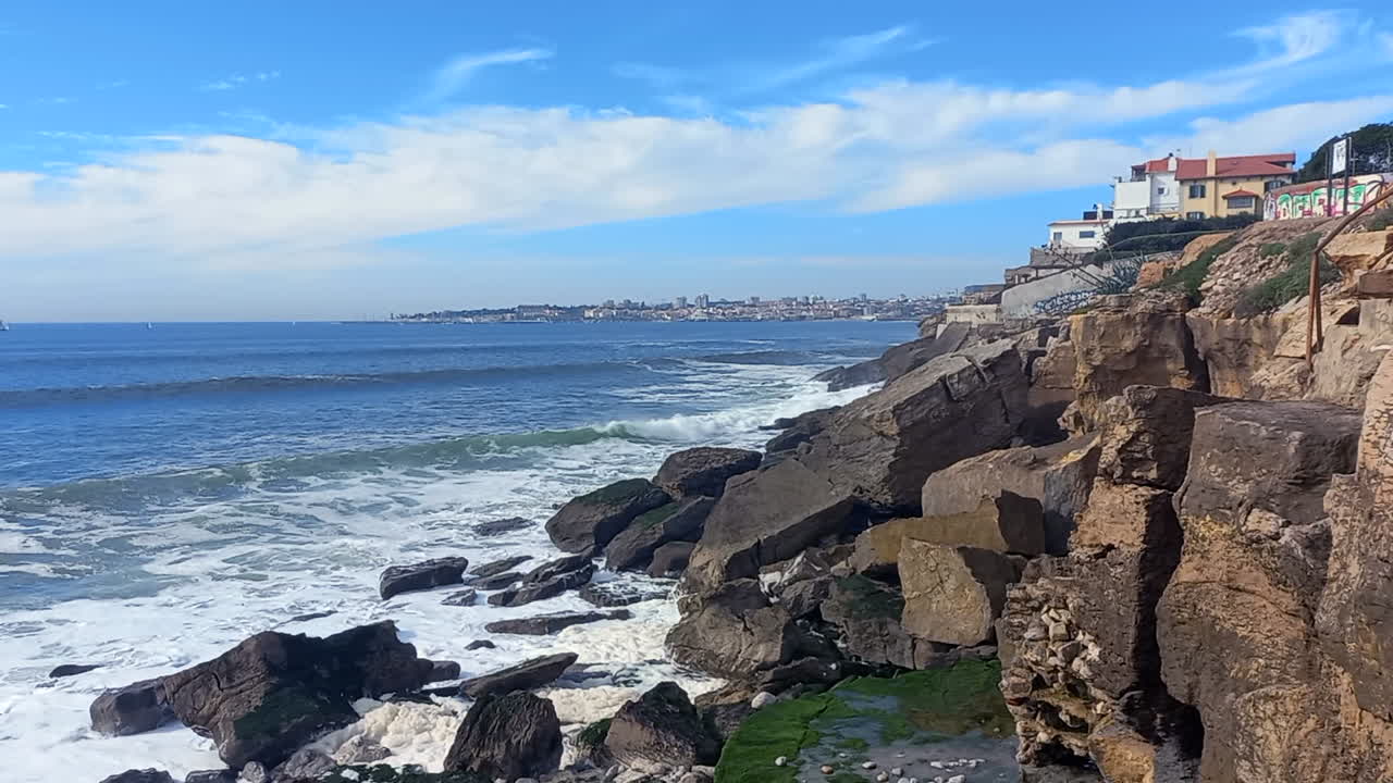 el mar y los barrancos con la ciudad y la bahía de cascais en el fondo, la belleza de un mar azul que golpea las rocas