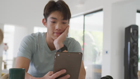 bored asian male teenager using tablet and sitting in living room