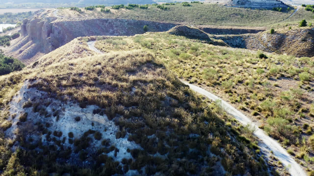 Trilha de mountain bike na savana espanhola, vista aérea em movimento para frente durante o pôr do sol, sem pessoas.