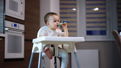 relaxed little kid eating fruit puree from plastic tube. sweet kid enjoying baby food from pack. low angle view.