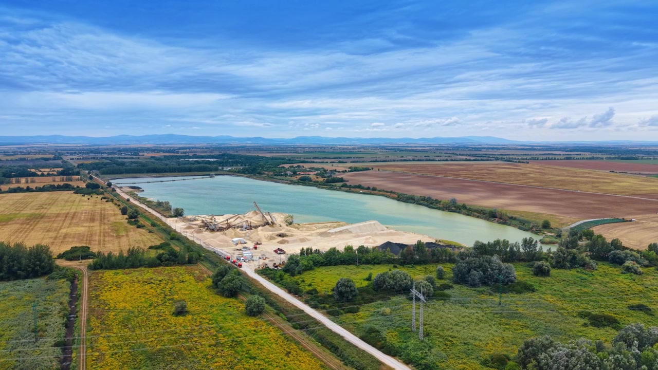 Vue aérienne lointaine d'une carrière de sable et des champs environnants. Une mine à ciel ouvert se trouve à côté d'un lac artificiel turquoise.