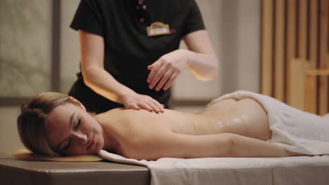 mujer encantadora se está relajando y disfrutando del masaje en el salón de spa masajista profesional está acariciando la espalda