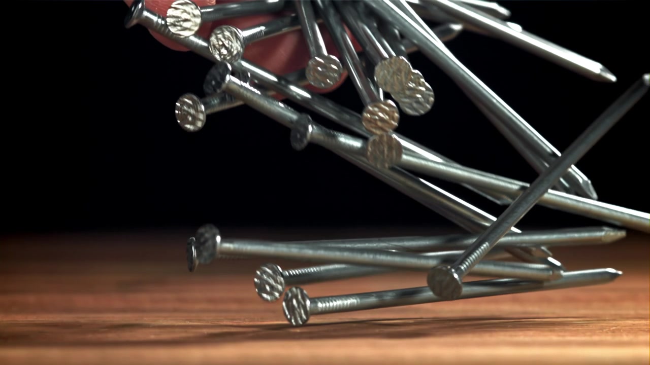 Primo piano di chiodi metallici che cadono al rallentatore sul legno