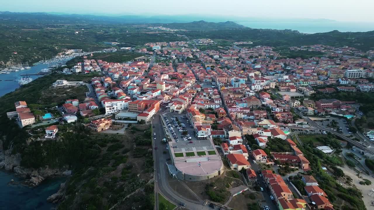 Aerial drone view of coastal town with red-tiled roofs and marina along Dalmatian Coast Croatia, showcasing urban layout, boats, and surrounding green hills under clear daylight