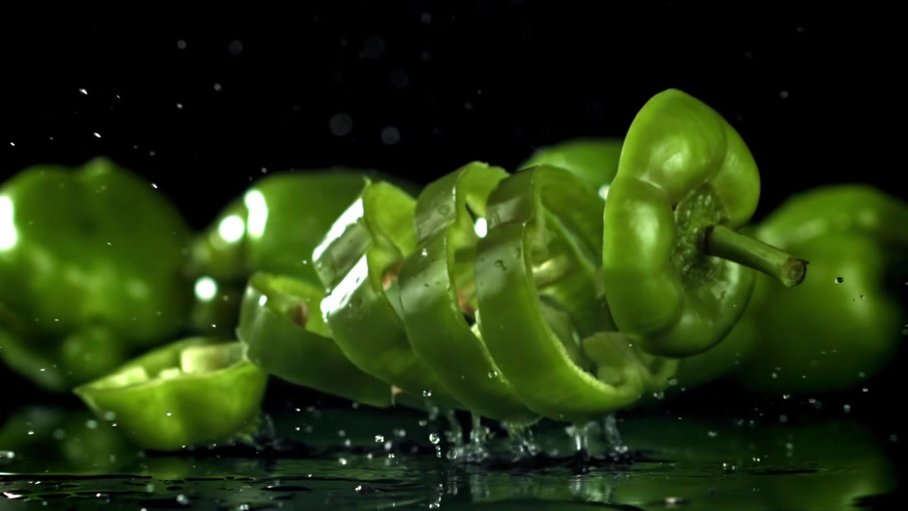 Sakte film: Skiver av grønn paprika spruter på en våt overflate.