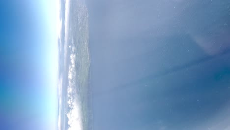 Aerial-view-of-blue-sky-and-ocean-and-land-from-plane-window-in-clear-weather-near-coast,-vertical