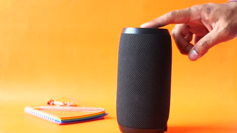 hand touching button of a black speaker on orange background