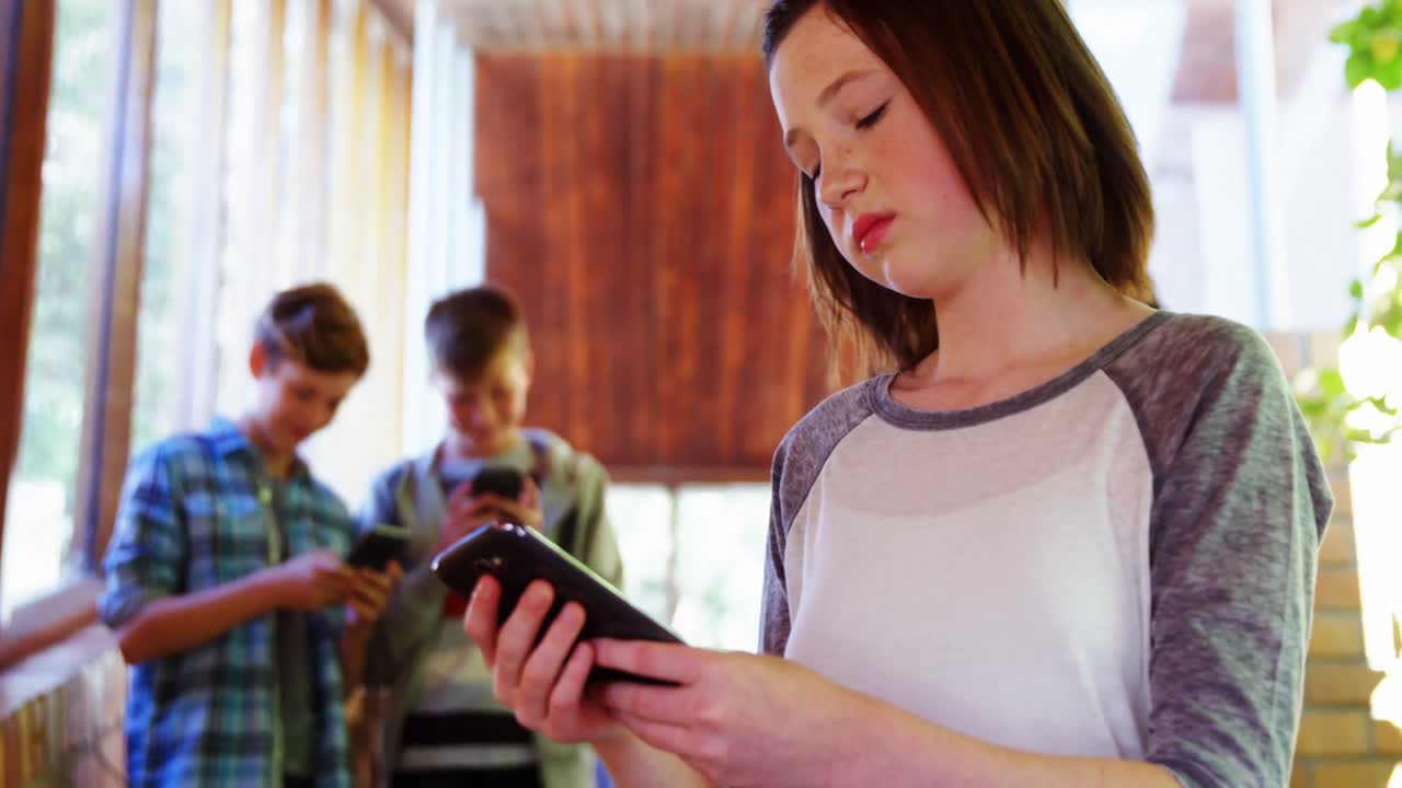 escolar usando el teléfono móvil en el pasillo de la escuela