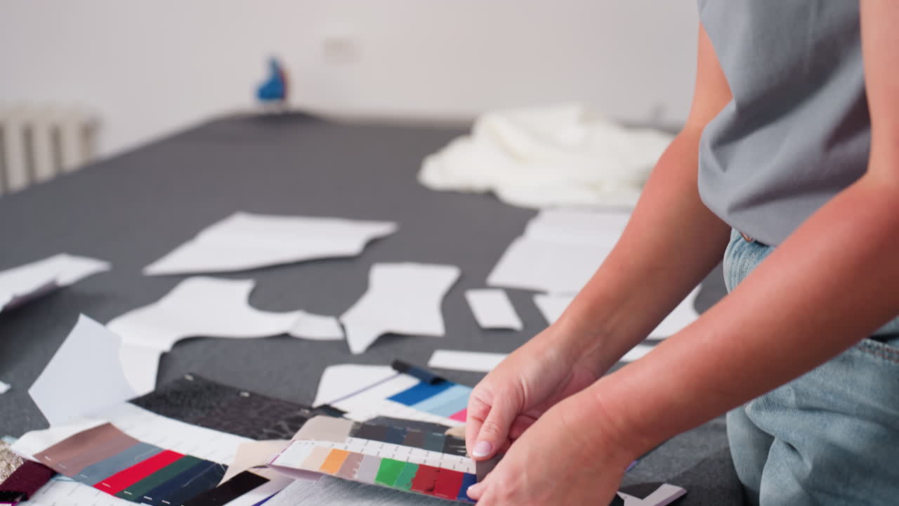 Seamstress arranging and matching colorful fabric pieces on large worktable surrounded by pattern sheets during creative fashion session in bright studio focused on color selection
