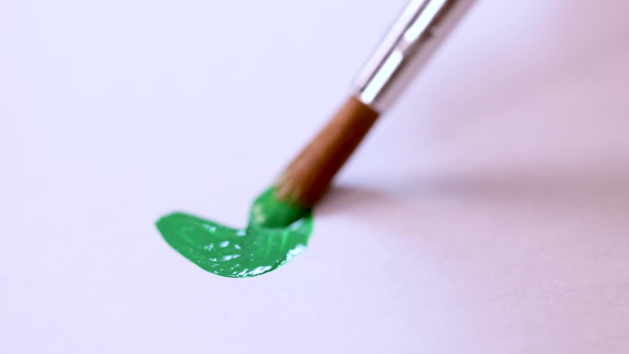 Close-up of hand painting green wavy line with brush on white paper, soft lighting